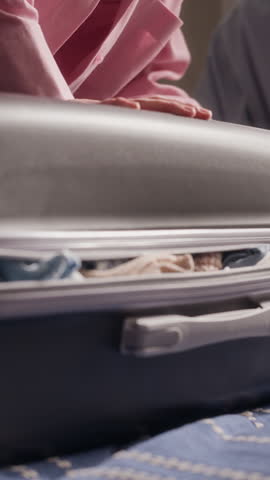 Vertical shot of woman stuffing clothes inside overpacked suitcase and zipping it closed. Clip is perfect for travel marketing campaigns and luggage brand promotions