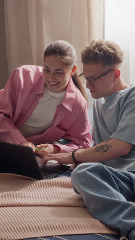 Vertical video of young adult Caucasian couple sitting on bed, using laptop and discussing online project together. Perfect for remote work, e-learning, or digital lifestyle marketing campaigns