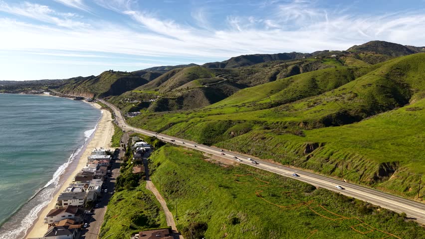Malibu Beach along PCH Highway overlooking Santa Monica Mountains with lush green grass on a clear sunny day. Vast coastal mountain, rolling hills and Pacific shore.