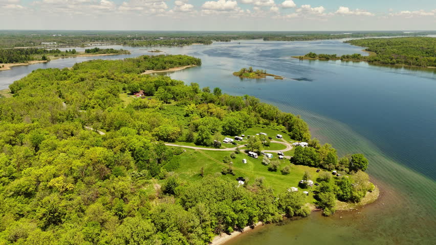 Aerial view of an island campground within the Upper Canada Migratory Bird Sanctuary in Ontario, Canada, featuring RVs and travel trailers surrounded by greenery and blue-green water.