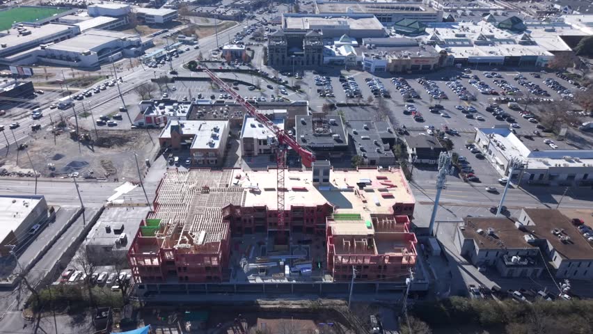 A large apartment complex under construction with wood framing, red crane, and urban surroundings - aerial tilt down reveal