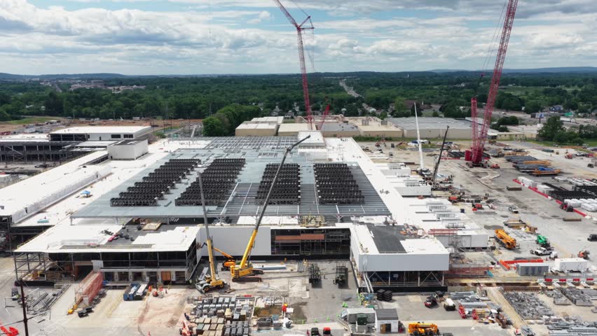 Data center campus in Lancaster shows rooftop cooling arrays, red and yellow cranes, steel-framed expansion, and stacked materials on sprawling site. Pennsylvania, USA. Aerial drone backwards shot