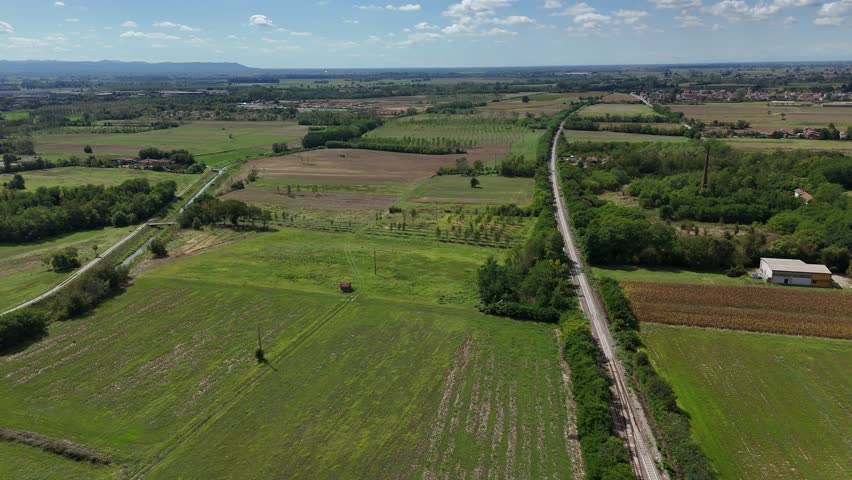 Agricultural fields, drainage corridors and rural roads form a geometric landscape across intensively cultivated farmland beneath distant mountain horizons, drone panning shot.