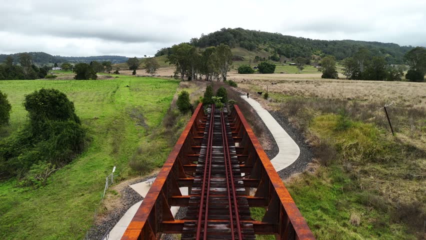 A female riding a modern e-bike travels under a disused rusty railway bridge part of a tourism cycle pathway. Drone view