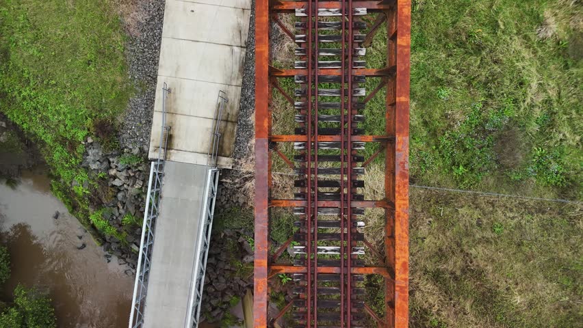 Northern Rivers rail trail bike path winding below an old rusty rail bridge spanning over a natural flowing creek and pedestrian bridge. Drone view