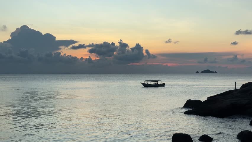 Footage of a boat sailing through the glowing golden waters near the Perhentian Islands as the sun sets over the South China Sea — a truly magical tropical moment, Terengganu, Malaysia.