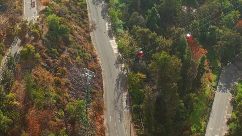 A telephoto aerial view of the Santiago cable car gondolas on San Cristobal Hill, with people jogging in the morning