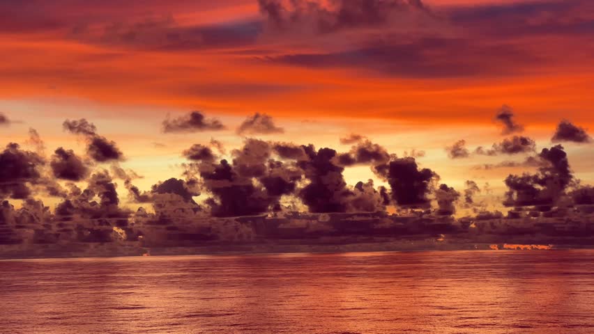 Dramatic sunset over the ocean with vibrant orange clouds reflecting on the water