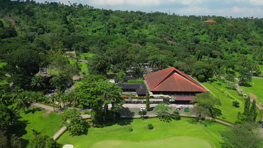 A tilt down aerial focusing on the clubhouse surrounded by tropical greenery, manicured lawns, and pathways, in Canlubang Golf and Country Club, Calamba Laguna, Philippines