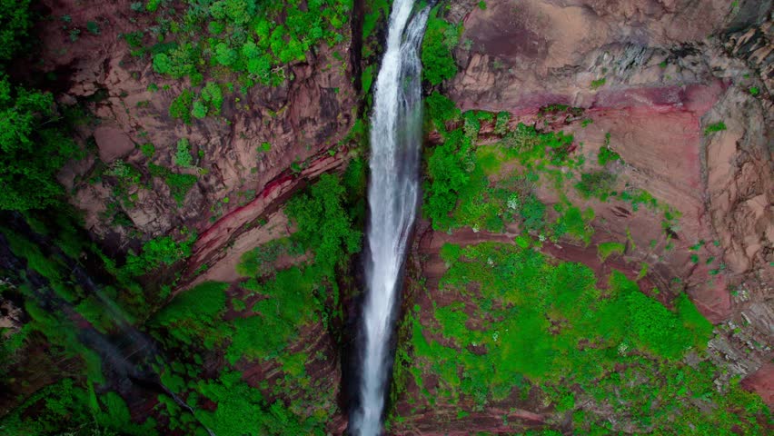 Vertical aerial zoom out highlighting a dramatic waterfall descending through steep rocky terrain.