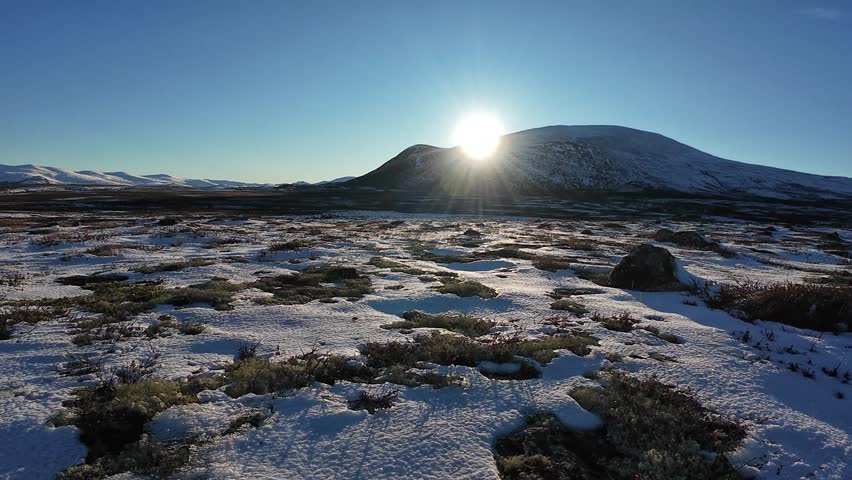 Bright sun rising over snowy mountains in Dovrefjell National Park