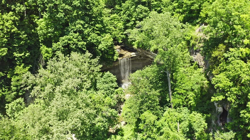 Small waterfall cascading over layered rock formations beneath a pedestrian bridge in Clifty Falls State Park, Indiana. The forested creek and rugged gorge create a scenic natural setting in southern Indiana.