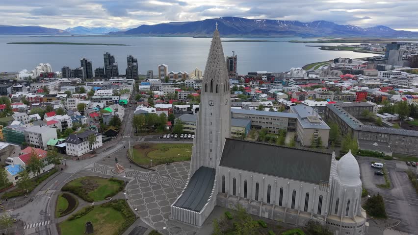 Dramatic aerial shot orbiting the iconic Hallgrimskirkja church, revealing the stunning panoramic cityscape of Reykjavik, Iceland