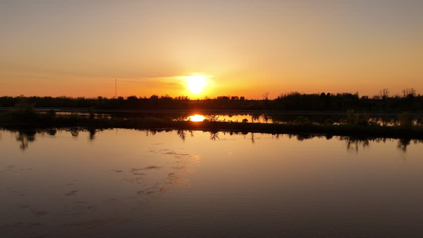 Silhouette of a couple cycling along a waterfront trail at sunset in Ontario, Canada, with the sun on the horizon and water surrounding the scenic pathway.