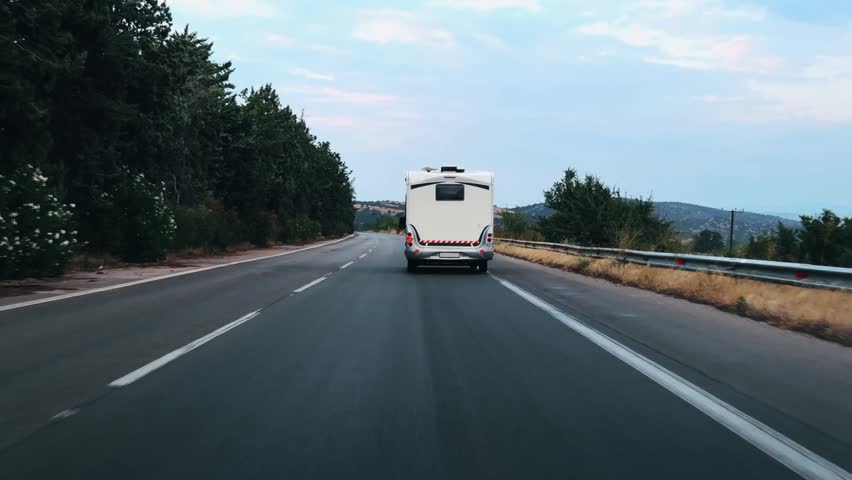 Traveler white camper van drive along a winding highway, flanked by lush trees and distant hills under a soft sky. The scene captures the essence of independent travel and spontaneous adventure on the open road.