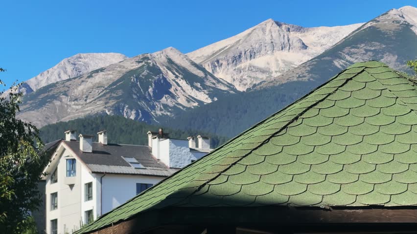 View of traditional buildings in Bansko, Bulgaria, set against the majestic peaks of the Pirin Mountain range under a clear blue sky.