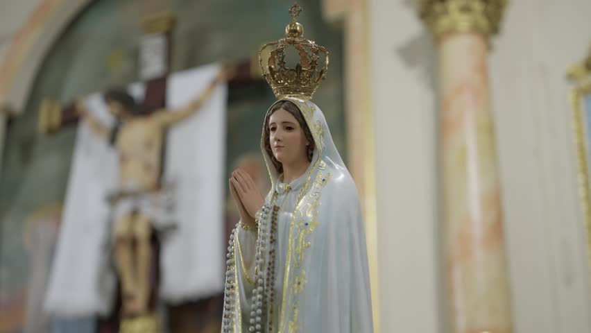 Crowned Virgin Mary statue praying with crucifix behind in Catholic church