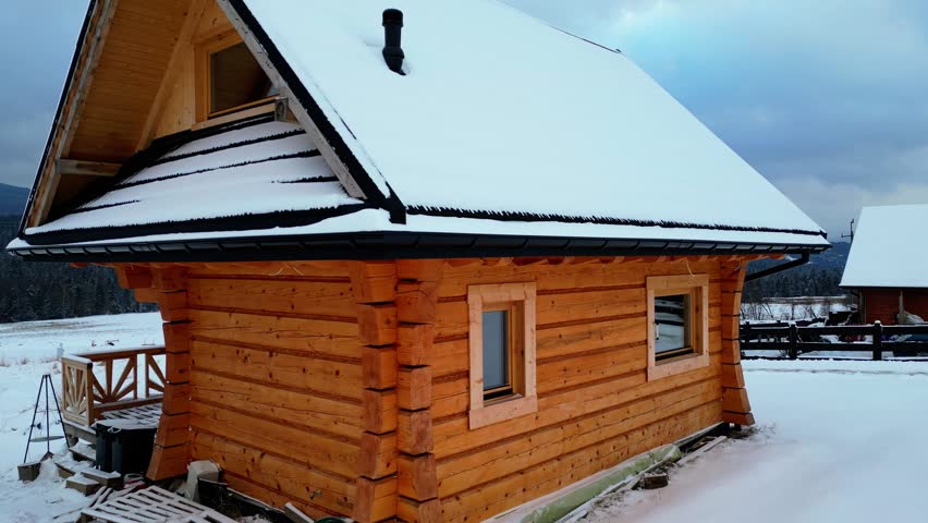 Full view of a snow‑covered wooden cabin surrounded by mountains. Dolly‑out and zoom‑in effect adds dramatic depth to the serene winter scenery
