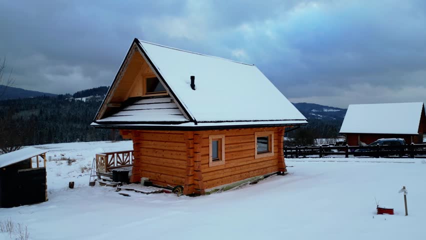 A handcrafted mountain cabin framed by snowy terrain and forested peaks. Drone cinematic dolly‑out and zoom‑in movement enhances the dramatic winter mood.