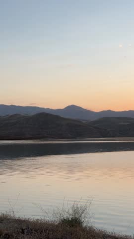 Scenic sunset over a calm lake with dramatic sun rays breaking through clouds over rolling hills