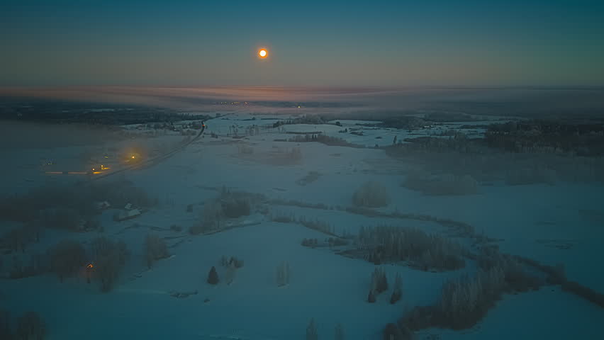 Time lapse hyperlapse aerial of moon rising over snowy rural landscape at dusk, car lights blurred