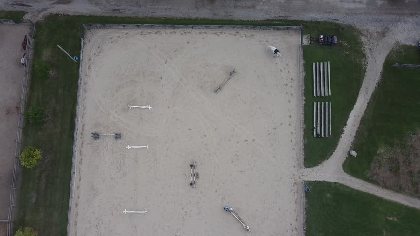 A descending drone shot from a birds eye view of an outdoor horse arena as an equestrian and their horse run and practice.