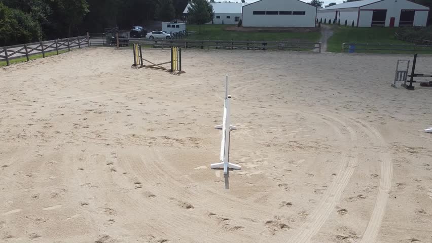 A drone shot flying along with a white horse and equestrian as they leap over multiple jumps in an outdoor arena.