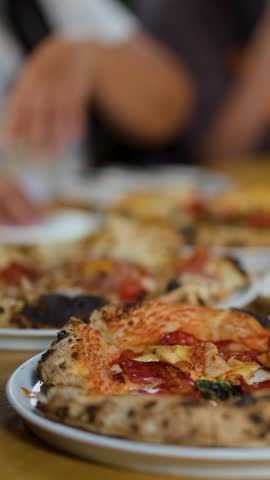 Close-up shot of hands taking a fresh pizza slice from a wooden restaurant table.