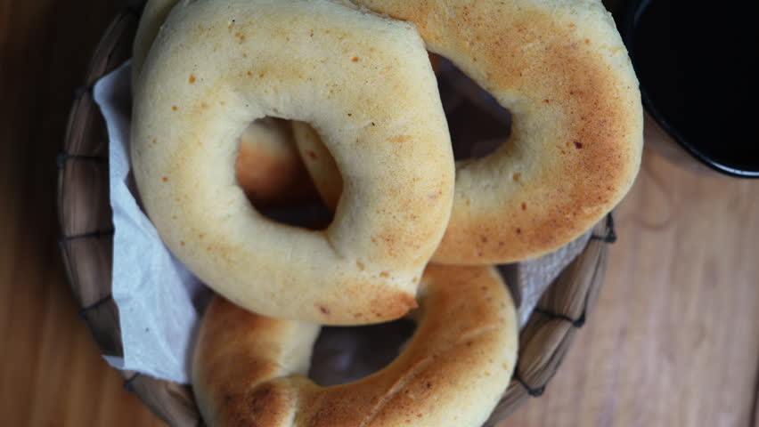 Detailed view of freshly baked pandebono rings in a rustic basket, paired with rich Colombian coffee, under soft, natural lighting. Captured in Cali, Valle del Cauca.