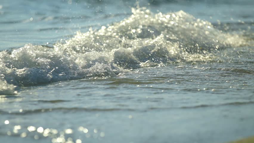 Ocean waves washing over yellow sand beach in sunlight.