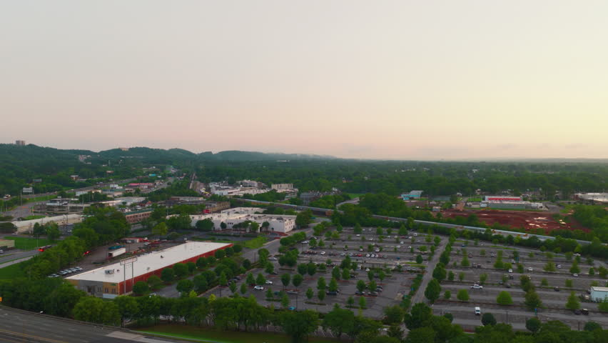 Panoramic aerial view of suburbs Birmingham Alabama featuring industrial buildings, parking lots, and a railway line surrounded by lush greenery under a soft morning sky.