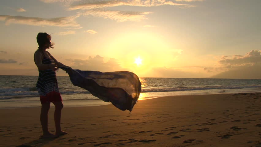 Silhouetted woman standing on sandy beach during sunset in Hawaii with sarong.