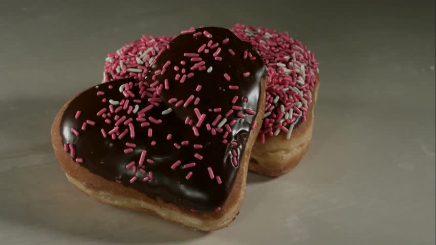 Chocolate heart donuts being covered with pink white sprinkles