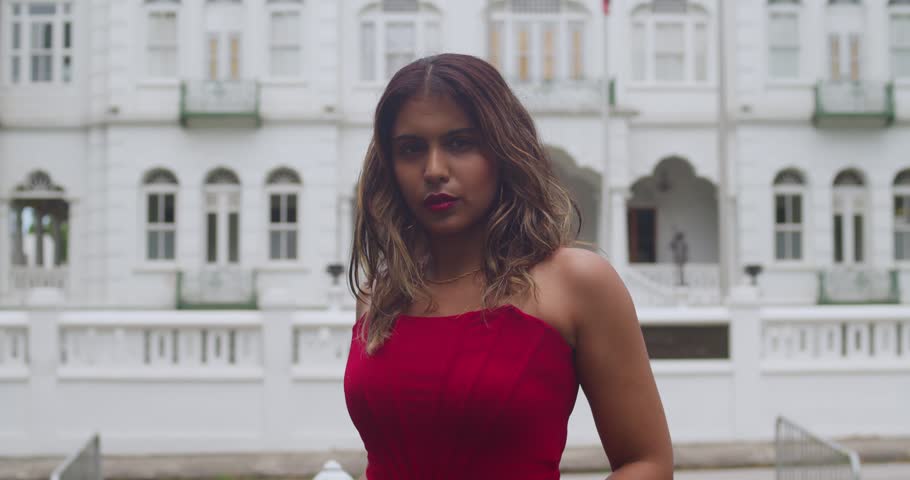 A girl in a bold red wrap dress walking a black horse along a historic stone wall in a vibrant tropical capital.