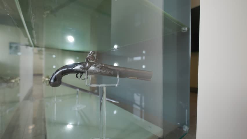 Vintage firearm from the 18th century exhibited on a stand behind protective glass in a museum