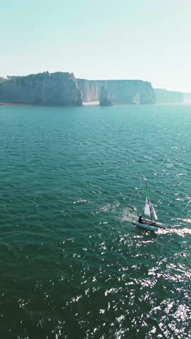 aerial footage of sailboats cruising along the coastline of Étretat, France. The majestic white cliffs and natural arches dominate the horizon while boats peacefully navigate the open sea under clear