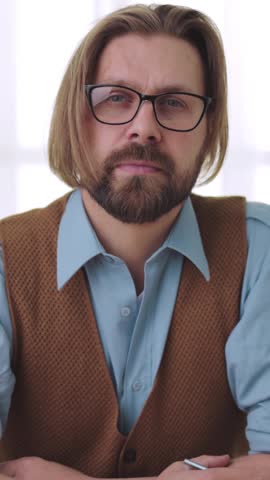 A man sits at a table, dressed in a blue shirt and brown vest, sharing thoughts on life.