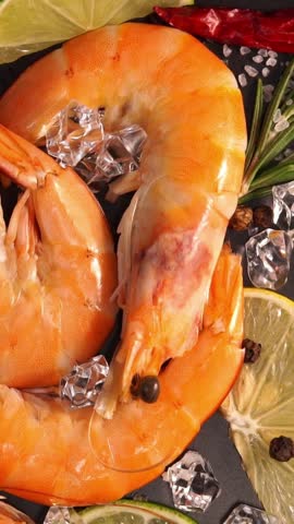 Top view of fresh raw shrimps in ice rotate on black tray. Seafood background close up. Food. Vertical shot