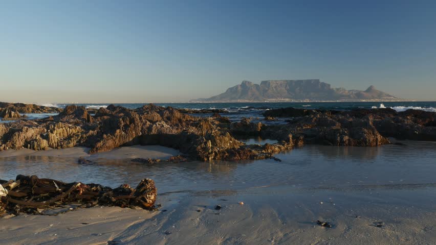 4K 25fps footage from Bloubergstrand showcasing the iconic Cape Town skyline with Table Mountain, Devil’s Peak and Lion’s Head across Table Bay under clear South African blue skies.