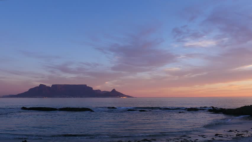 4K 25fps footage from Bloubergstrand showcasing the iconic Cape Town skyline with Table Mountain, Devil’s Peak and Lion’s Head across Table Bay under clear South African blue skies.