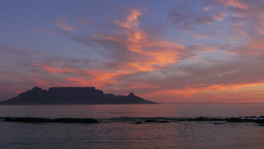 4K 25fps footage from Bloubergstrand showcasing the iconic Cape Town skyline with Table Mountain, Devil’s Peak and Lion’s Head across Table Bay under clear South African blue skies.
