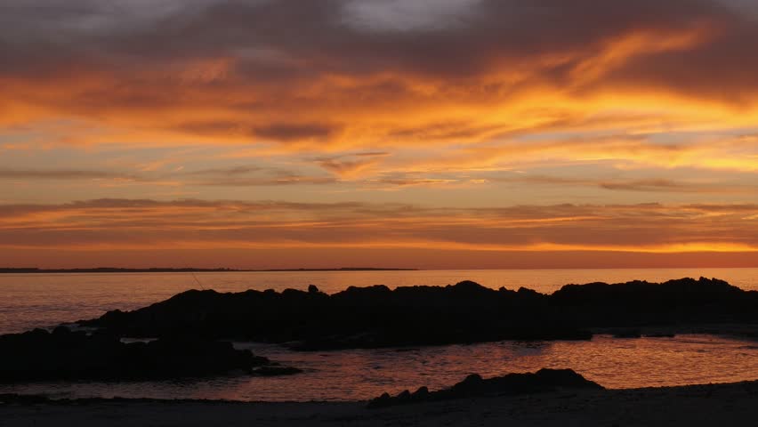 4K 25fps sunset footage from Bloubergstrand showing the rugged rocky coastline and distant Robben Island across Table Bay, bathed in warm golden light along Cape Town’s Atlantic shoreline.