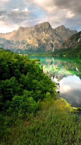 A stunning landscape featuring a crystal-clear turquoise lake reflecting majestic, rugged mountain peaks under a soft, cloudy sky at sunset.