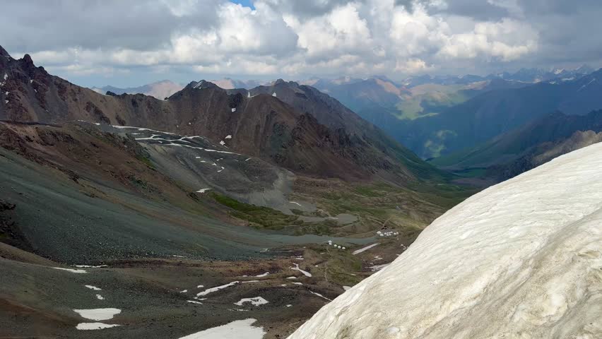 High alpine valley with scree slopes, snow patches and yurt camp