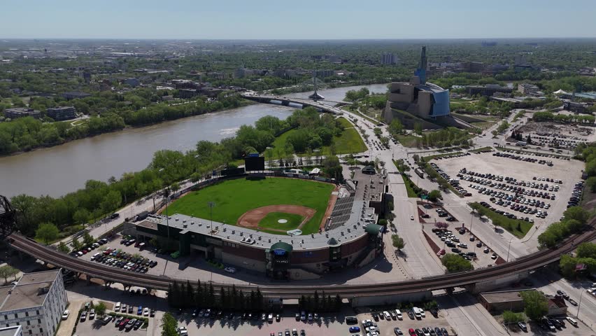 Winnipeg, Manitoba. Static drone shot showing Goldeyes stadium, Red River, and Canadian Museum for Human Rights with nearby roads and traffic on a clear sunny summer day.