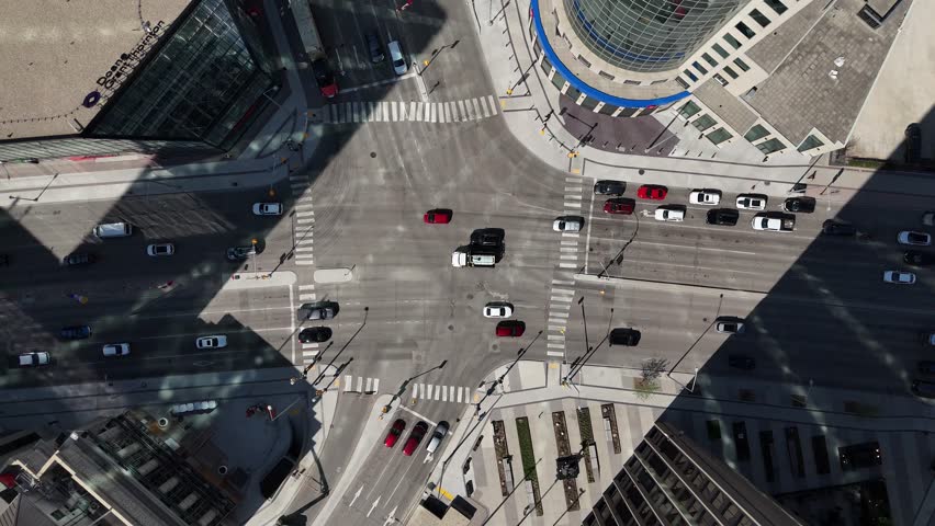 Portage Avenue and Main Street intersection in downtown Winnipeg, Manitoba. Direct overhead drone shows moving traffic and crosswalks with strong building shadows on a sunny summer day.