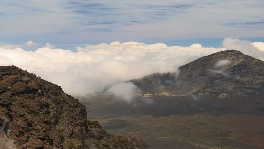 Haleakala Crater rim overlooking volcanic terrain, mountain slopes and a dense cloud layer in Haleakala National Park. Static daytime establishing shot