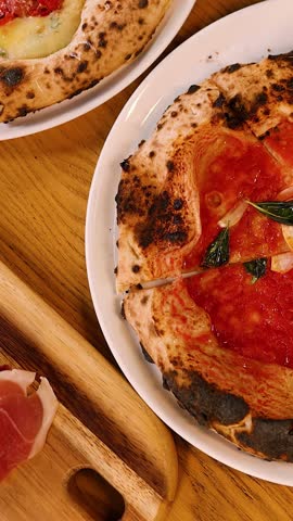 Overhead view of diners sharing wood-fired margherita pizza with tomato sauce and fresh basil.