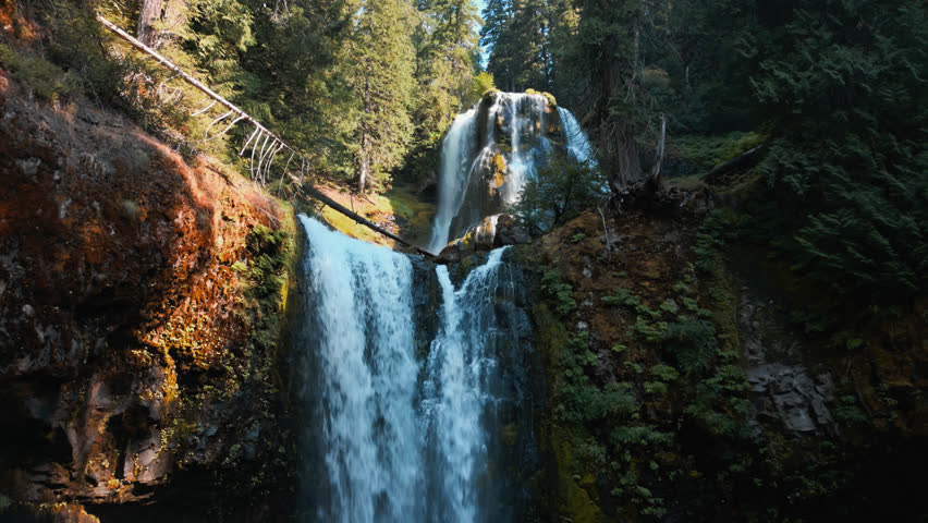 Orbital tilted up view around Falls Creek Falls upper and lower falls in shaded forest canyon surrounded by rocky surfaces and forest trees