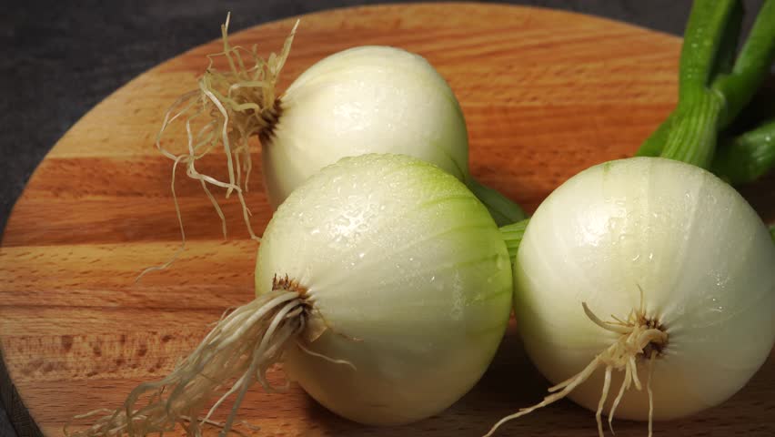  Clean organic fresh onion bulbs with water droplets turning on a rustic wooden background.